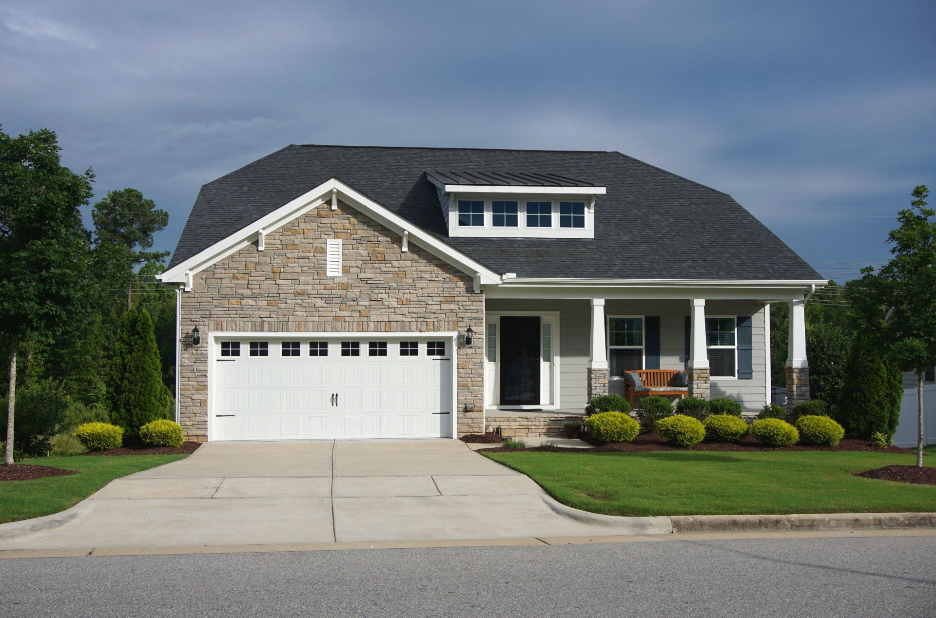 Suburban house with stone facade, white garage, and front porch under a cloudy sky