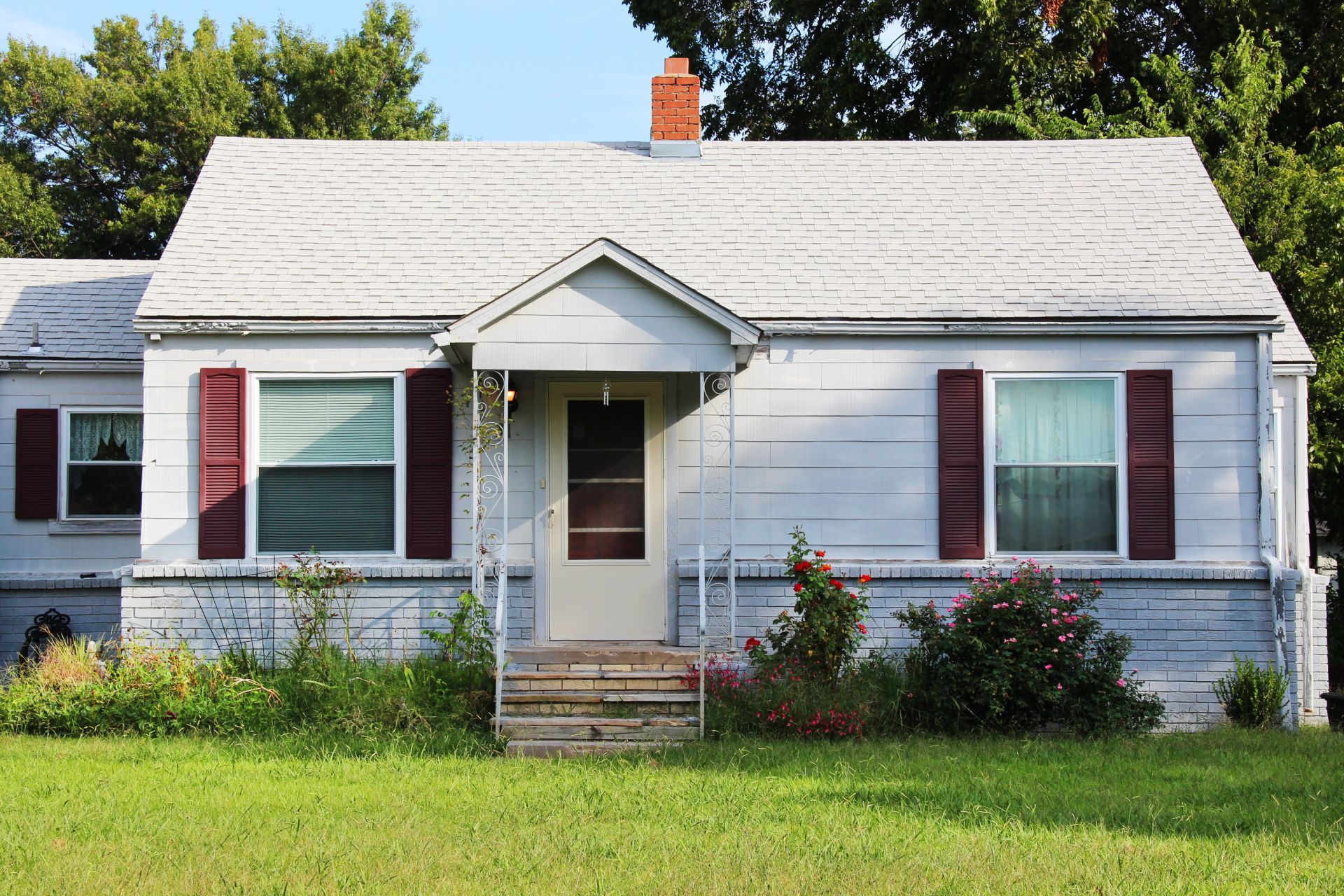 Small white house with red shutters, front porch, and green lawn under a bright sky