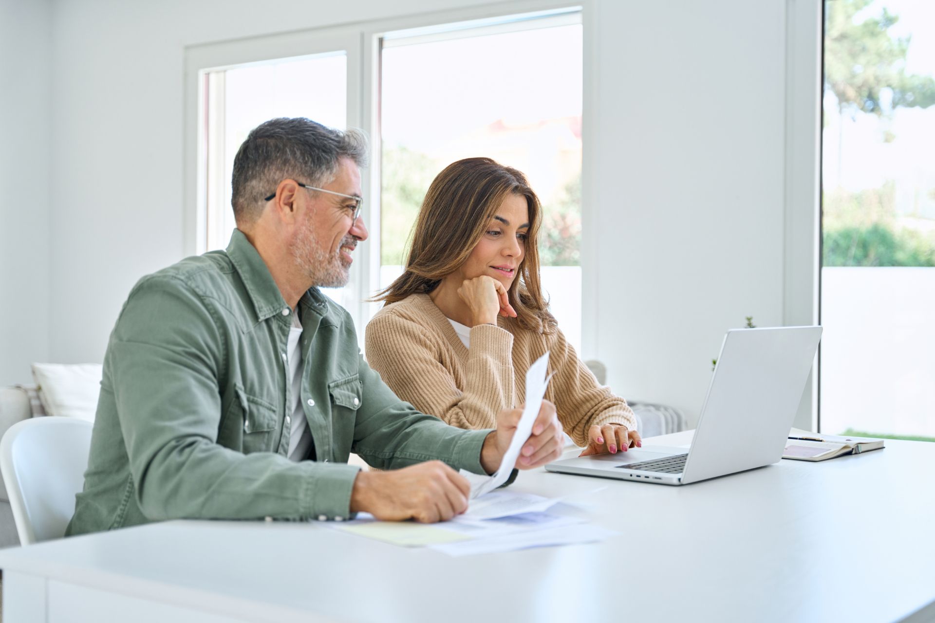 Two coworkers reviewing documents on a laptop in a bright office