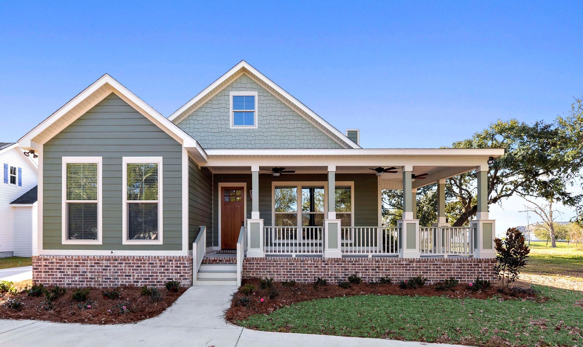 Gray farmhouse-style house with white trim, front porch, and brick foundation on a landscaped lawn