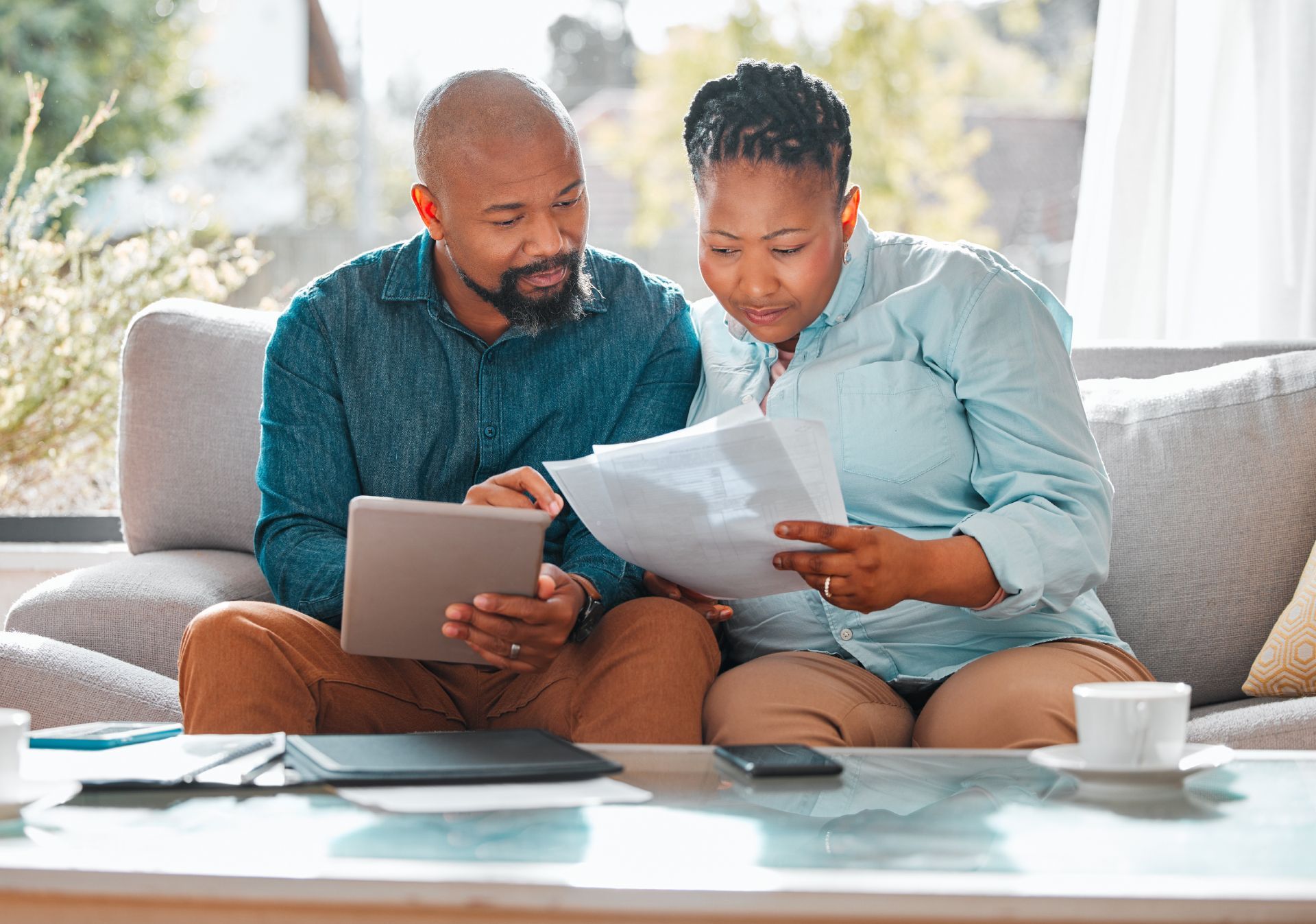 Two people on a couch reviewing papers and a tablet in a bright living room