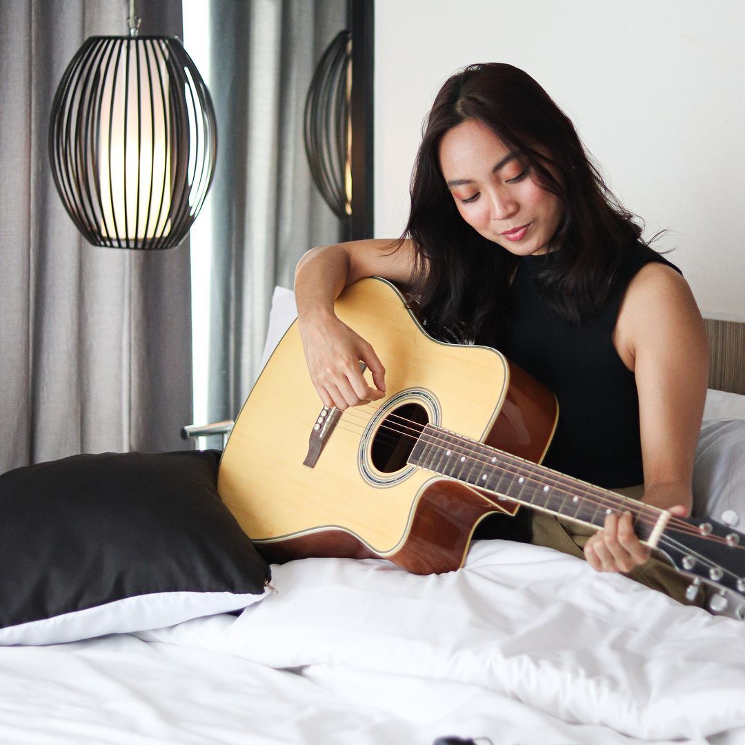 Woman playing acoustic guitar on hotel bed at Y2 Residence Makati
