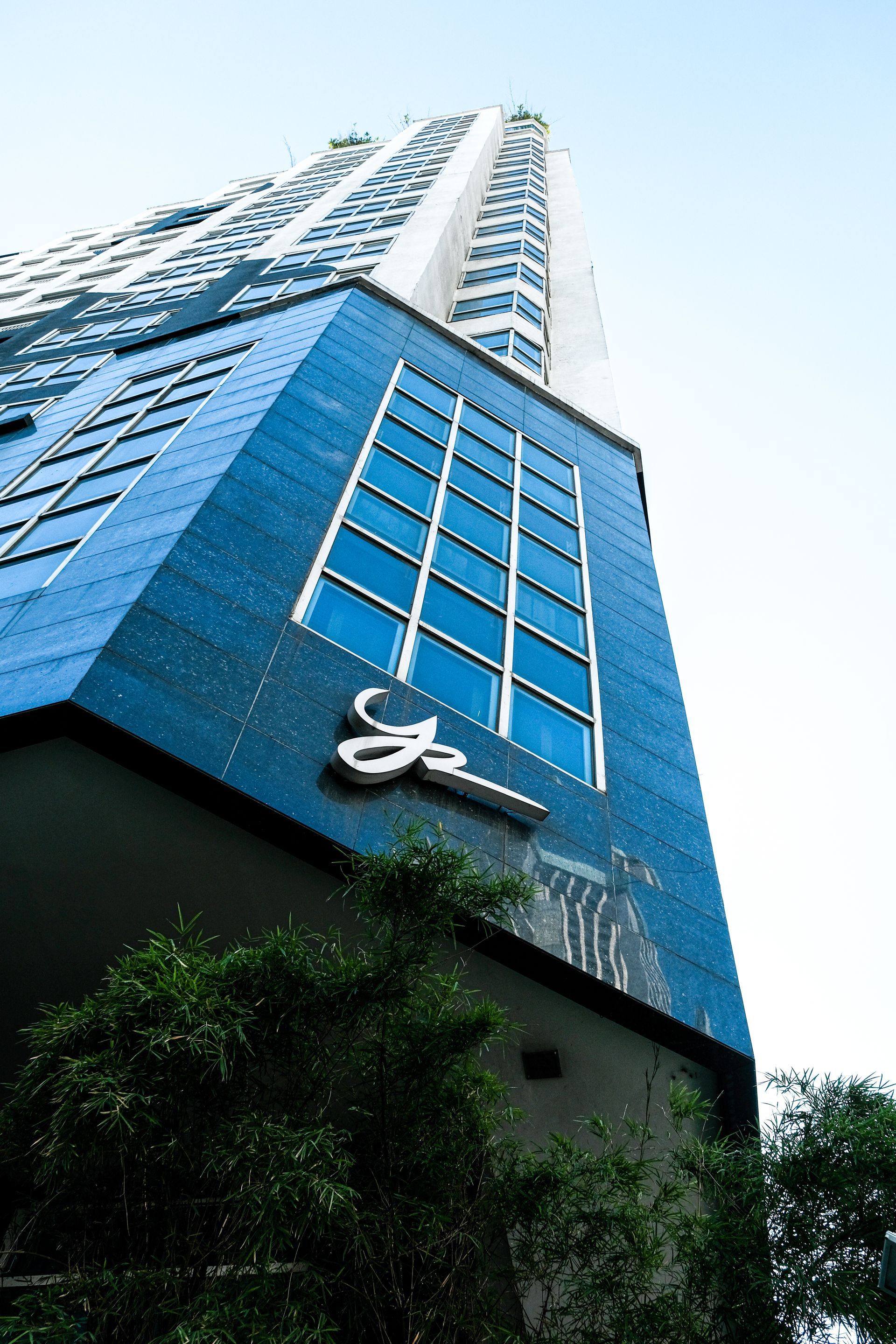 Low-angle view of a blue-and-white high-rise building with greenery at the base