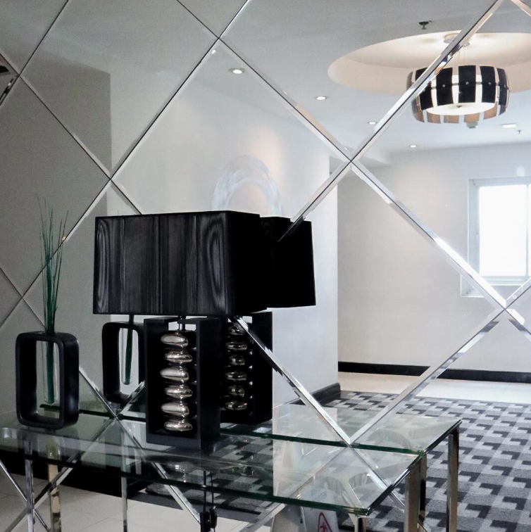 Mirror wall with diamond-shaped panels reflecting a hallway, table with lamp and vase.