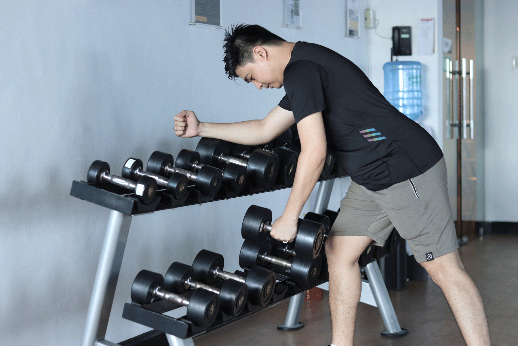 Person lifting a dumbbell from a rack in a gym, performing a bent-over row.