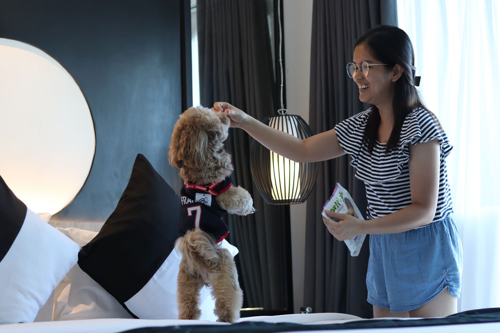 Guest feeding a treat to her small poodle on the bed of a pet-friendly room at Y2 Residence Hotel Makati