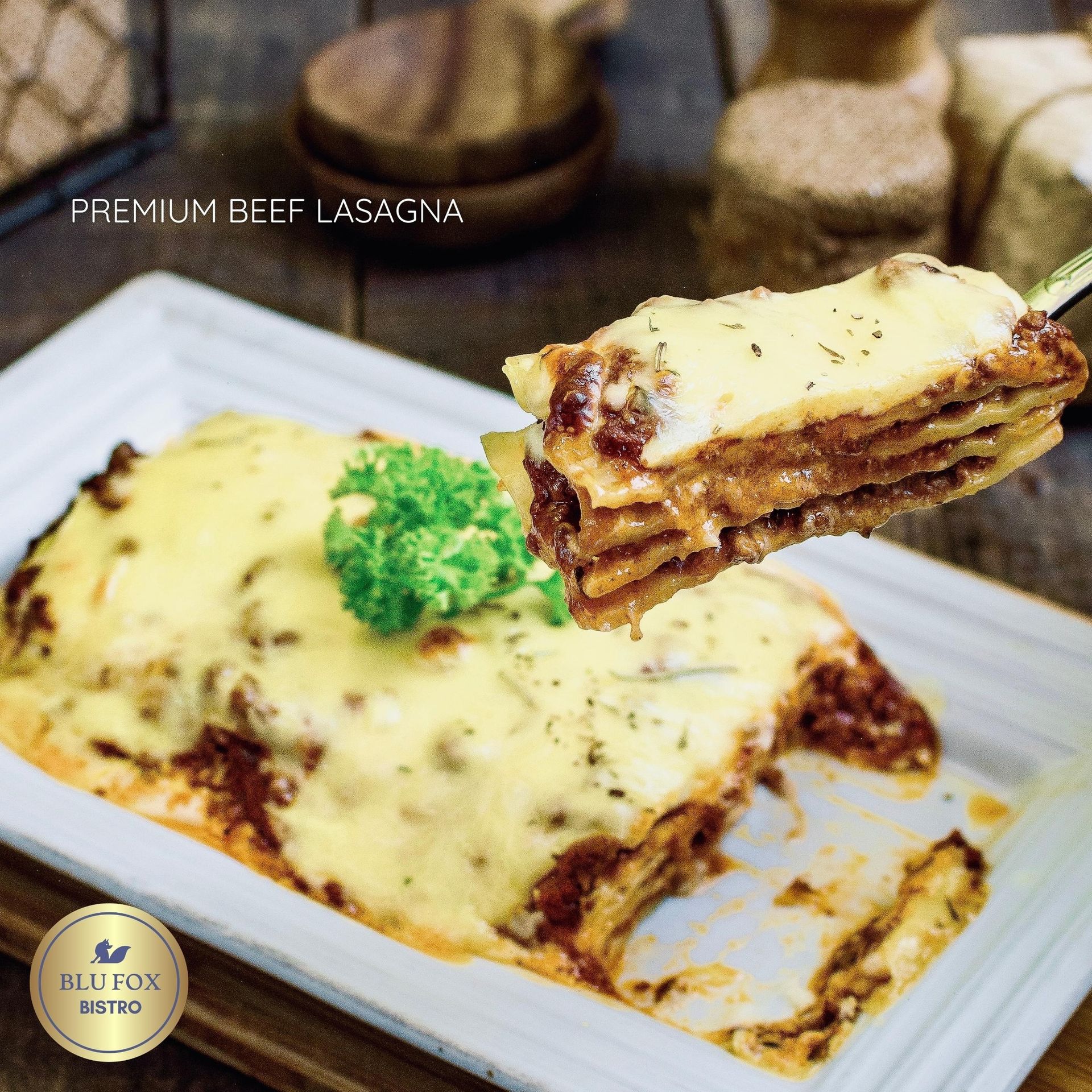 Premium beef lasagna on a white rectangular plate; a portion lifted by a fork, topped with cheese and a green broccoli.