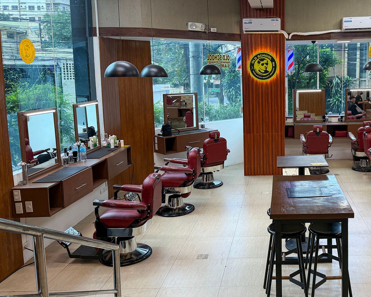 Empty barbershop with red chairs, mirrors, and wood-paneled walls by large front windows.