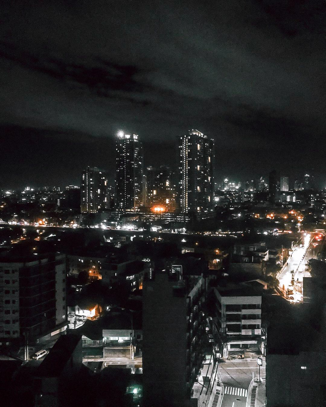 City skyline at night, with illuminated buildings against a dark cloudy sky.