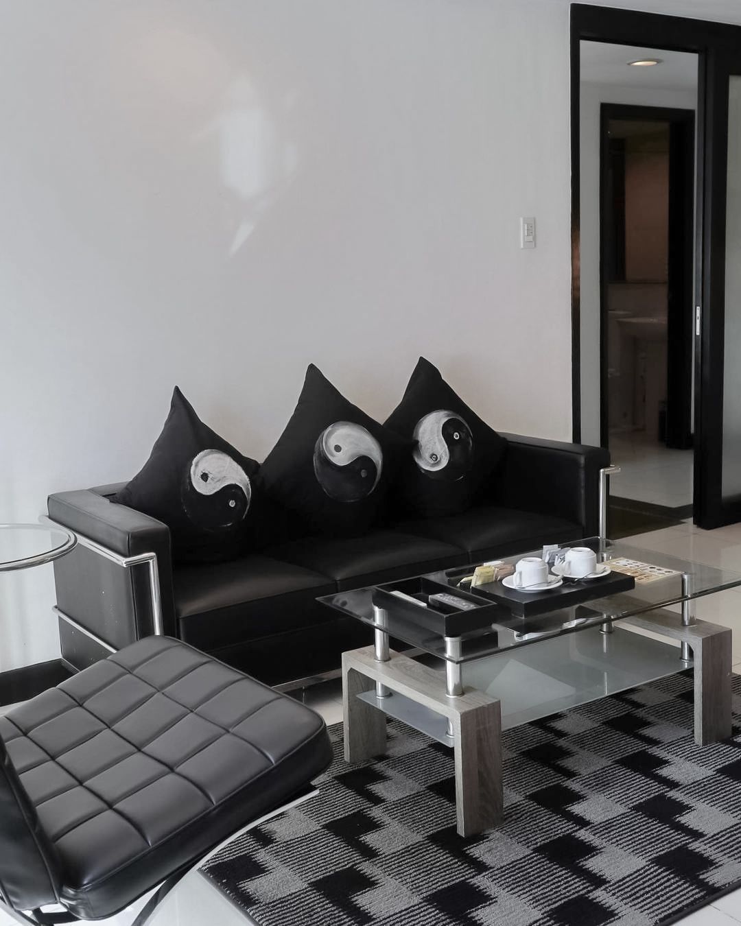 Black leather couch with yin yang pillows, glass coffee table, and patterned rug.