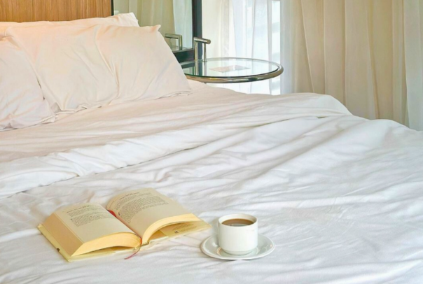 Bed with open book and coffee cup on white sheets.