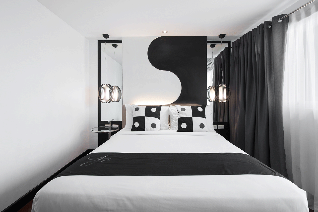 Black and white bedroom with bed, decorative headboard, and hanging lights.