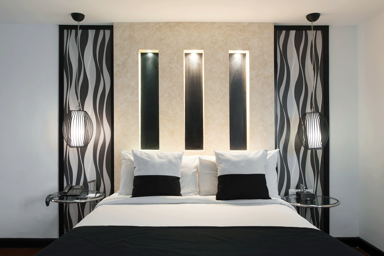 A modern bedroom featuring a bed centered against a wall with black-and-white patterned panels and three backlit niches.