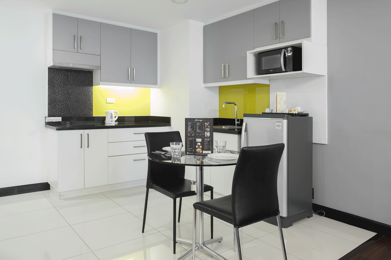 Small kitchen with gray and white cabinets, black countertop, microwave, and small dining table.