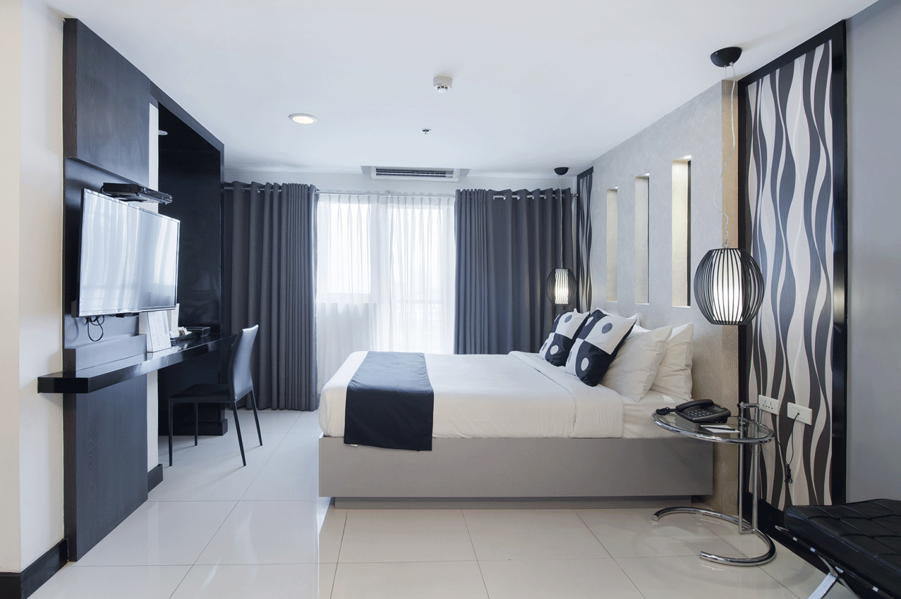 Modern hotel room with bed, desk, TV, and decorative paneling in gray and black.