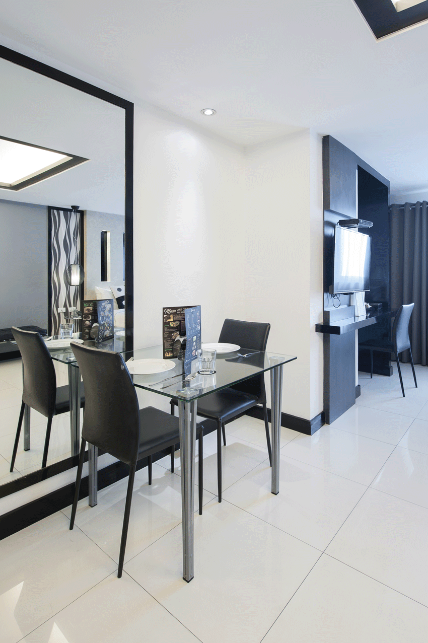 Modern dining area with glass table, black chairs, and a large wall mirror on white tiled flooring