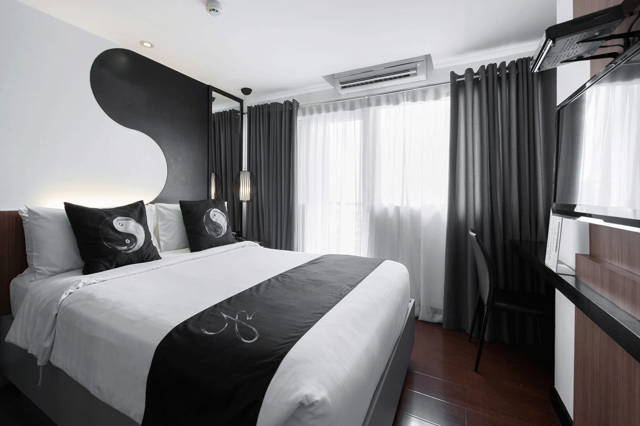 A modern bedroom with a black and white theme, featuring a bed with monochromatic bedding, dark curtains, and a desk.