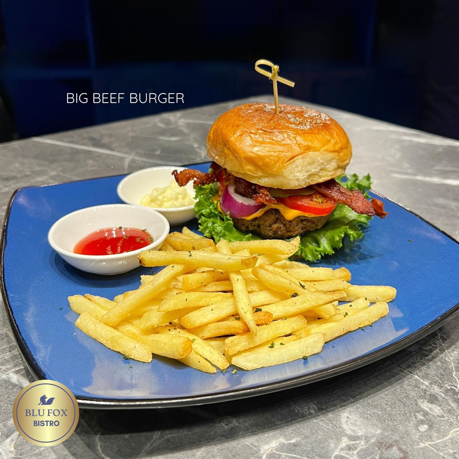 Big beef burger with fries and sauces on a blue plate.