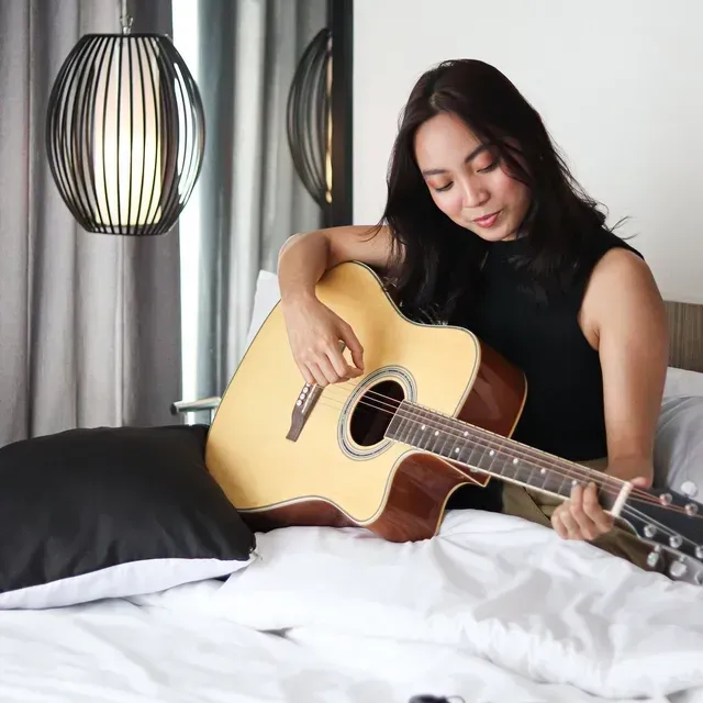 Guest playing acoustic guitar on bed at Y2 Residence Hotel, Poblacion Makati