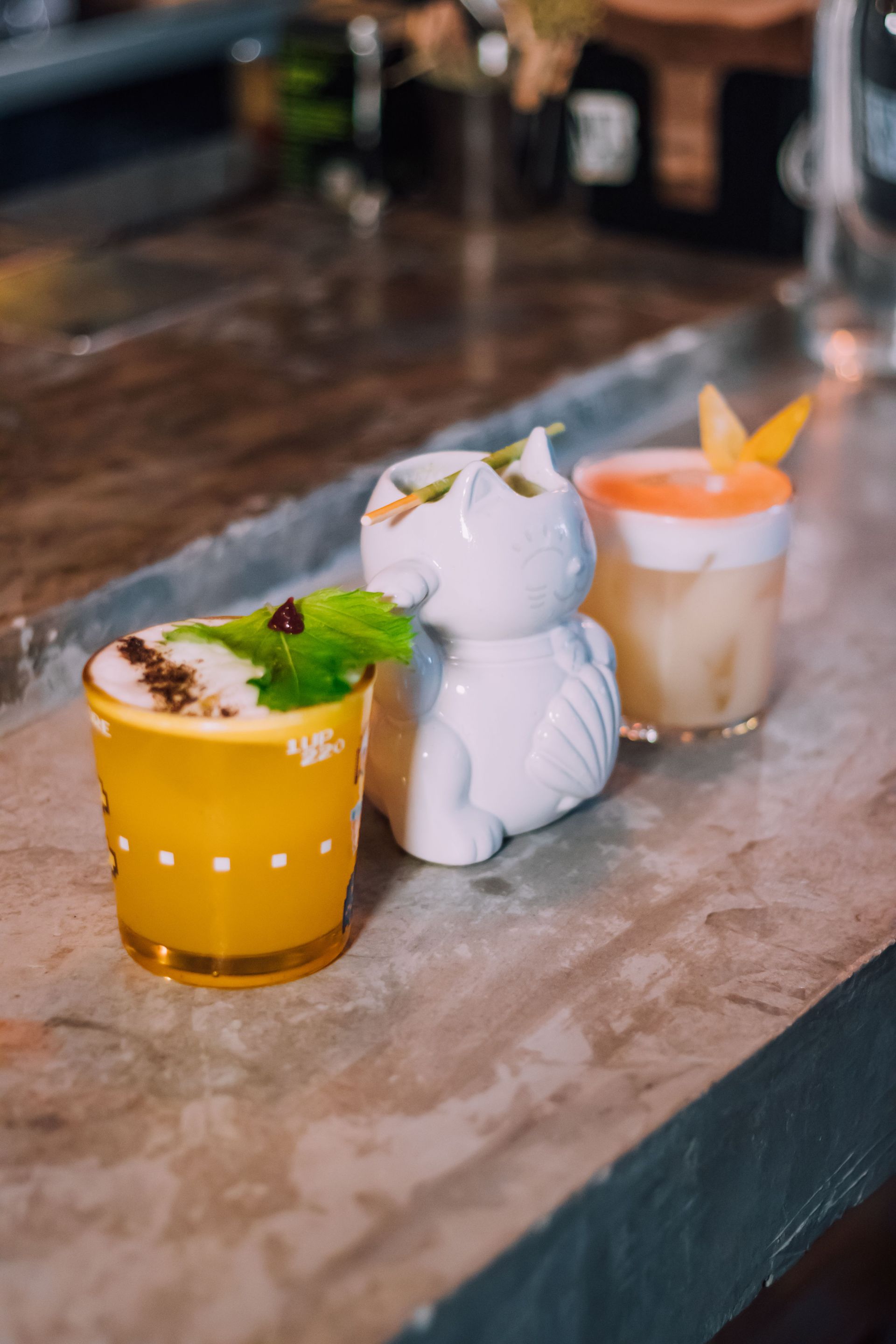 Three colorful cocktails in animal-shaped glasses on a bar counter