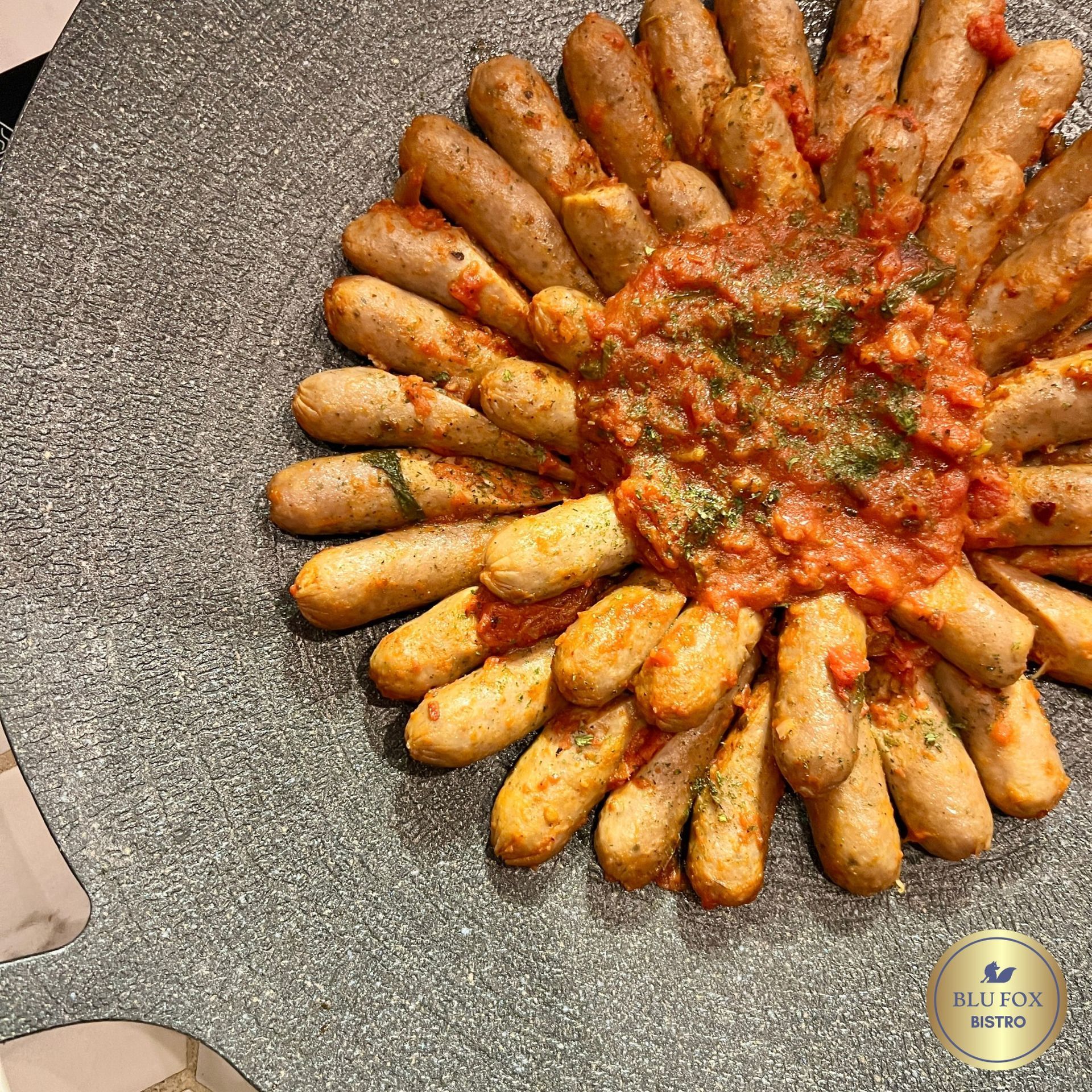 Sausages arranged in a circle, topped with tomato sauce, on a textured grey plate.