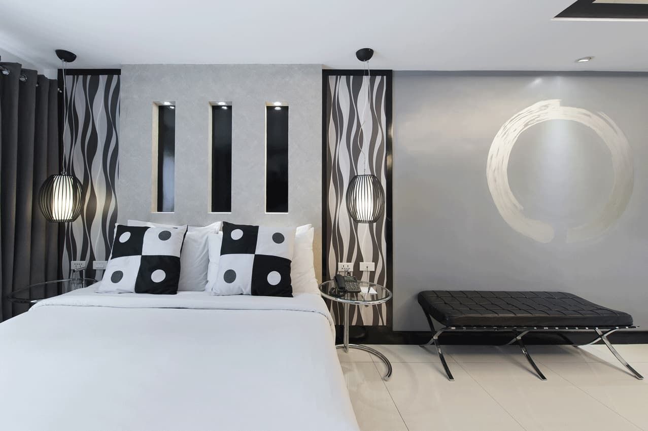 Modern bedroom with black-and-white decor, double bed, and a black bench against a gray wall.