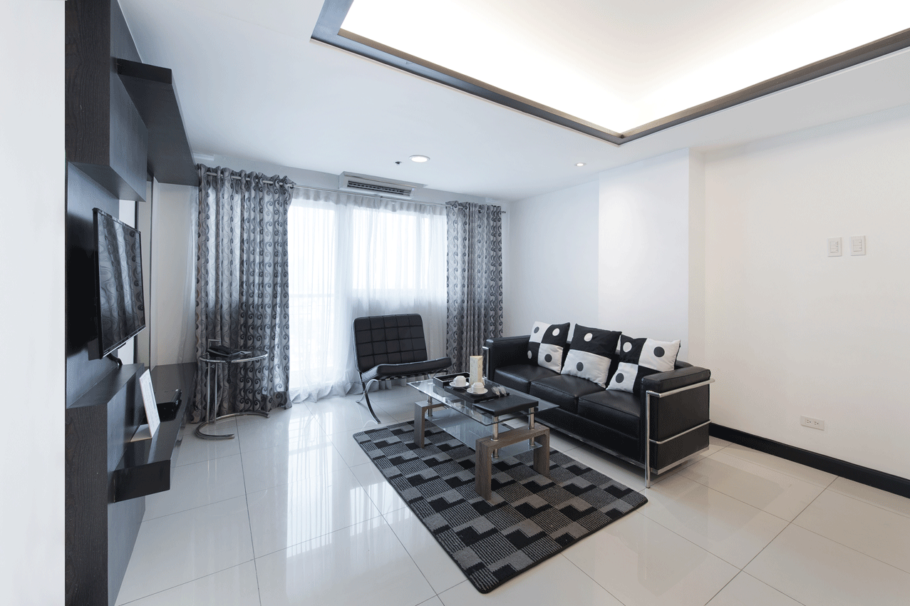 Modern living room with black-and-white sofa, glass coffee table, TV, and bright curtains over glossy tile floor