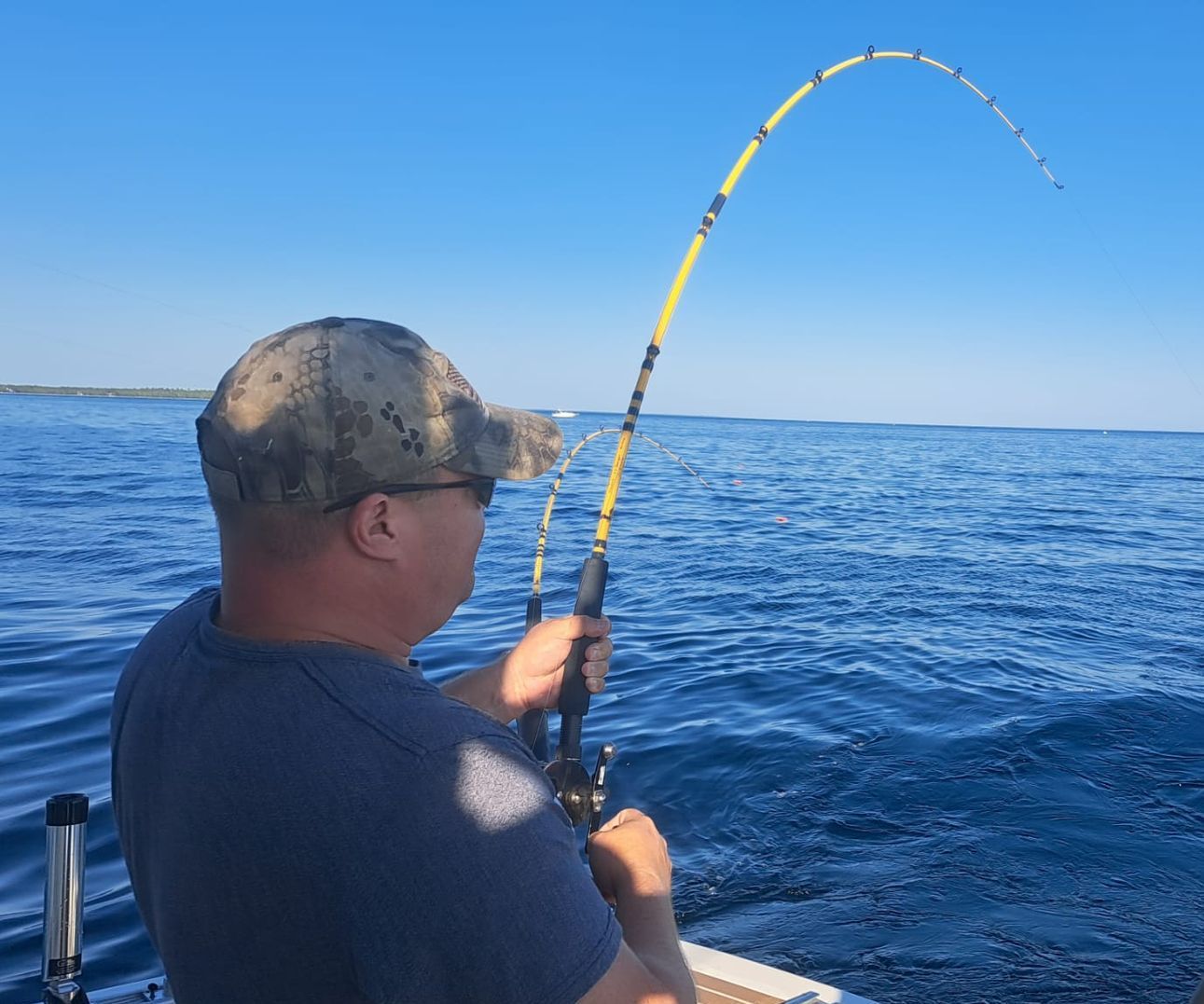 Angler on a boat holding a bent fishing rod over blue ocean water