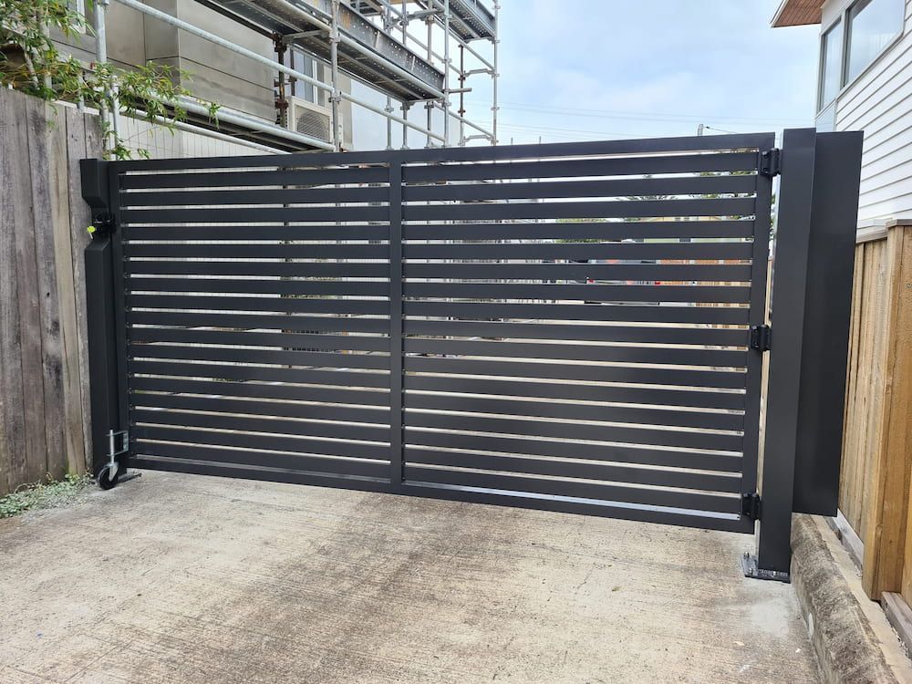 A Black Gate is Sitting on Top of a Concrete Driveway Next to a Wooden Fence — SCF Industries Pty Ltd in Albion Park, NSW