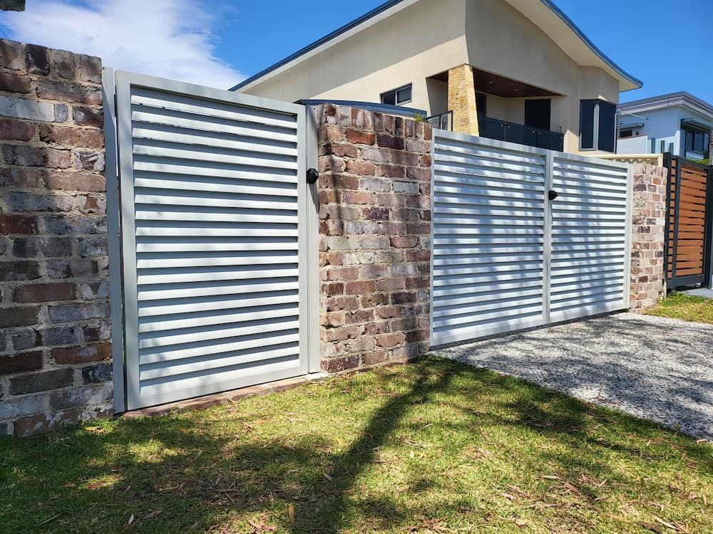A White Gate is Sitting Next to a Brick Wall in Front of a House — SCF Industries Pty Ltd in Shellharbour, NSW