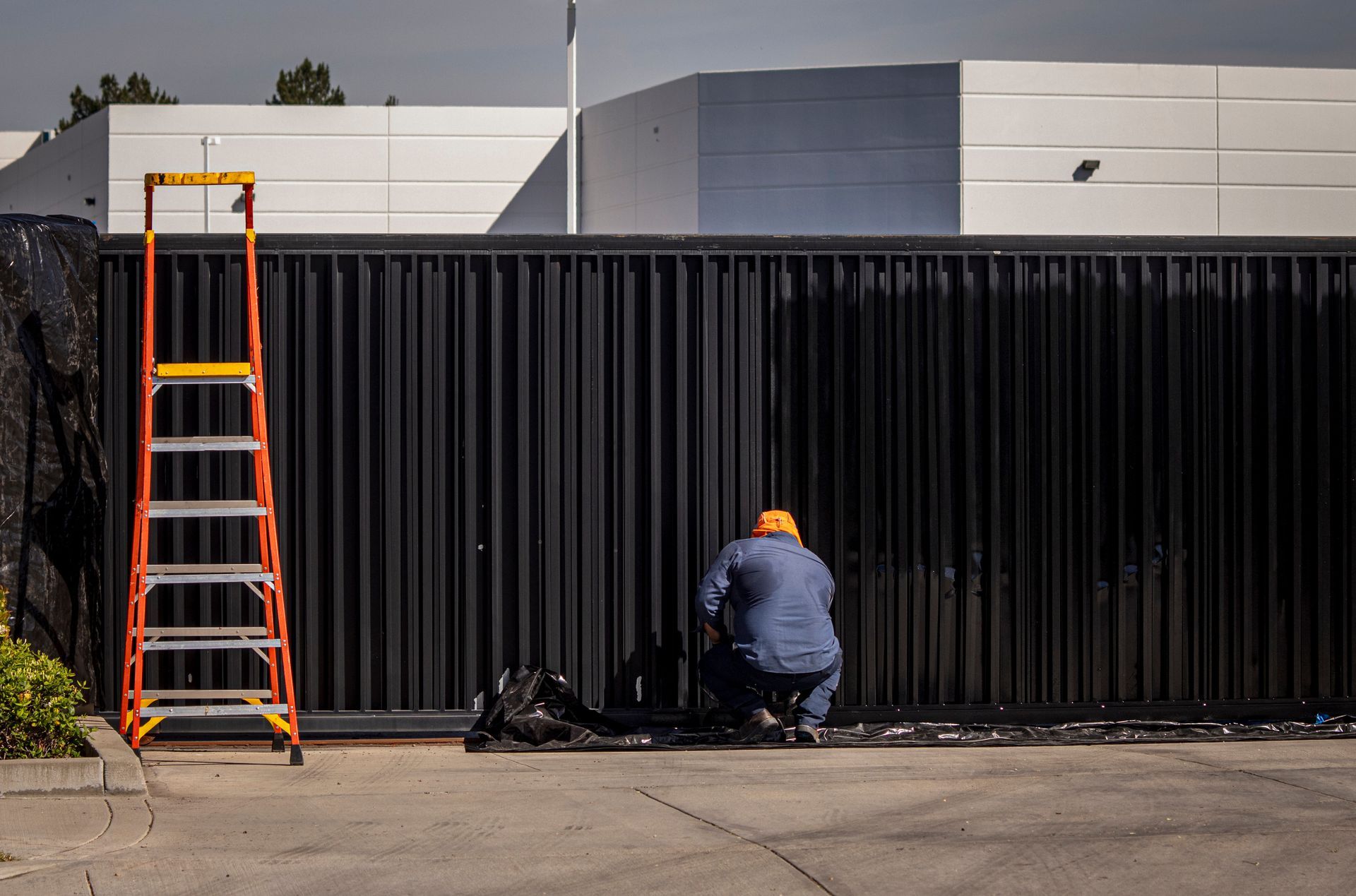 Painter in blue coveralls painting a white exterior wall from a scaffold