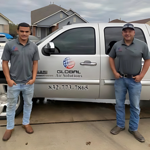Two men in gray shirts stand by a silver truck with 