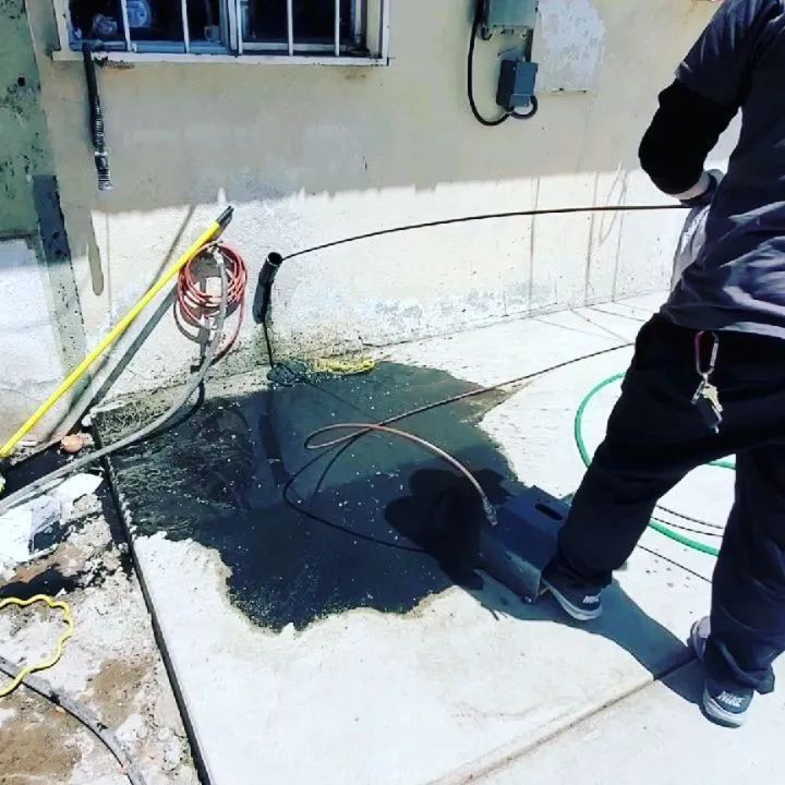 Person standing near a large black spill on a concrete patio beside a building wall and hoses