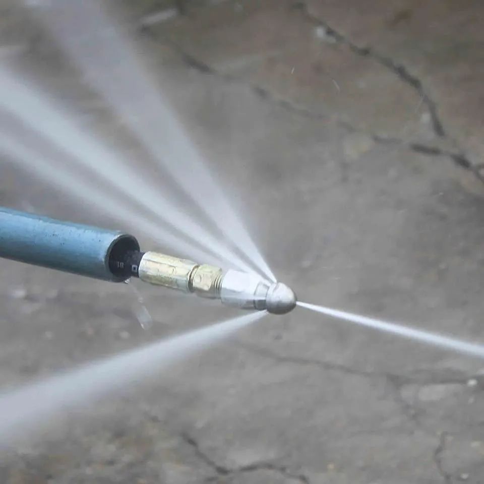 Close-up of a pressure washer nozzle spraying water in multiple jets onto concrete.