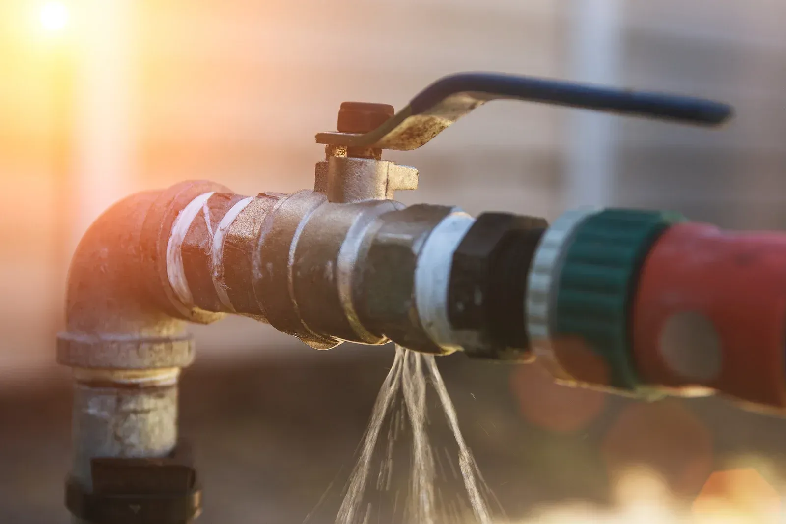 Leaky outdoor faucet spraying water. Bright sunlight.