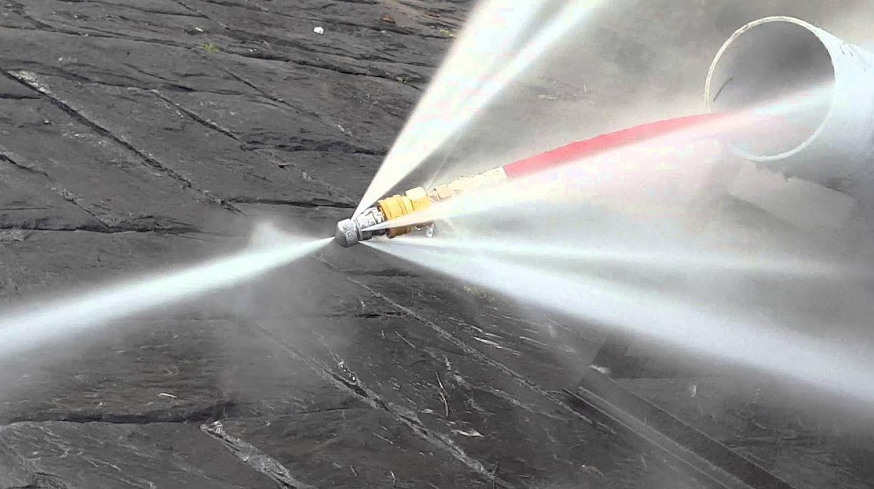 Water spraying from a nozzle onto brick pavement; a white pipe is to the right.