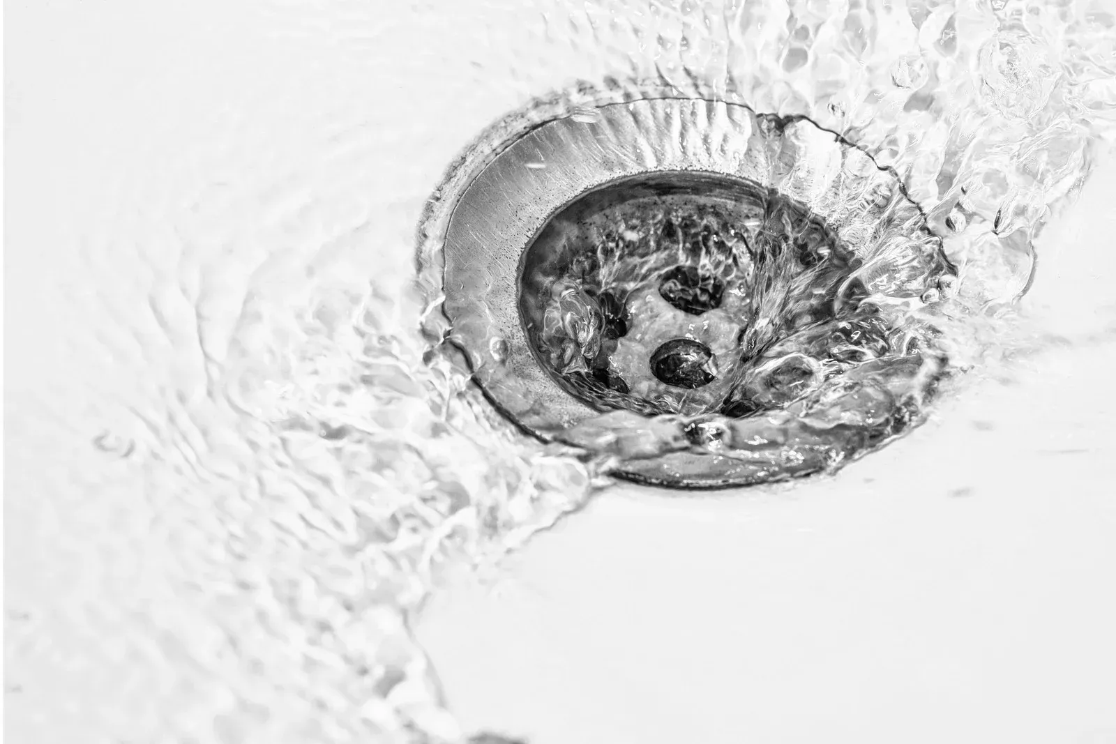 Person unclogging a bathtub drain with a snake tool and a plunger in a white tub.