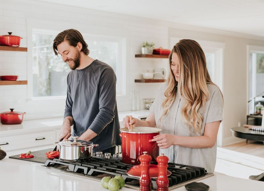 Two people cooking in a bright kitchen, stirring pots on a gas stove.