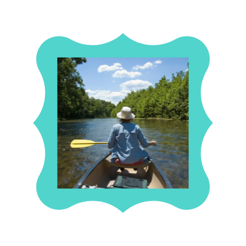 A woman in a hat is paddling a canoe on a river.
