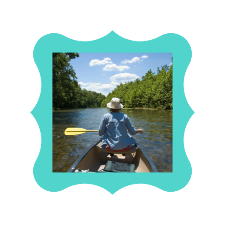 A woman in a hat is paddling a canoe on a river.