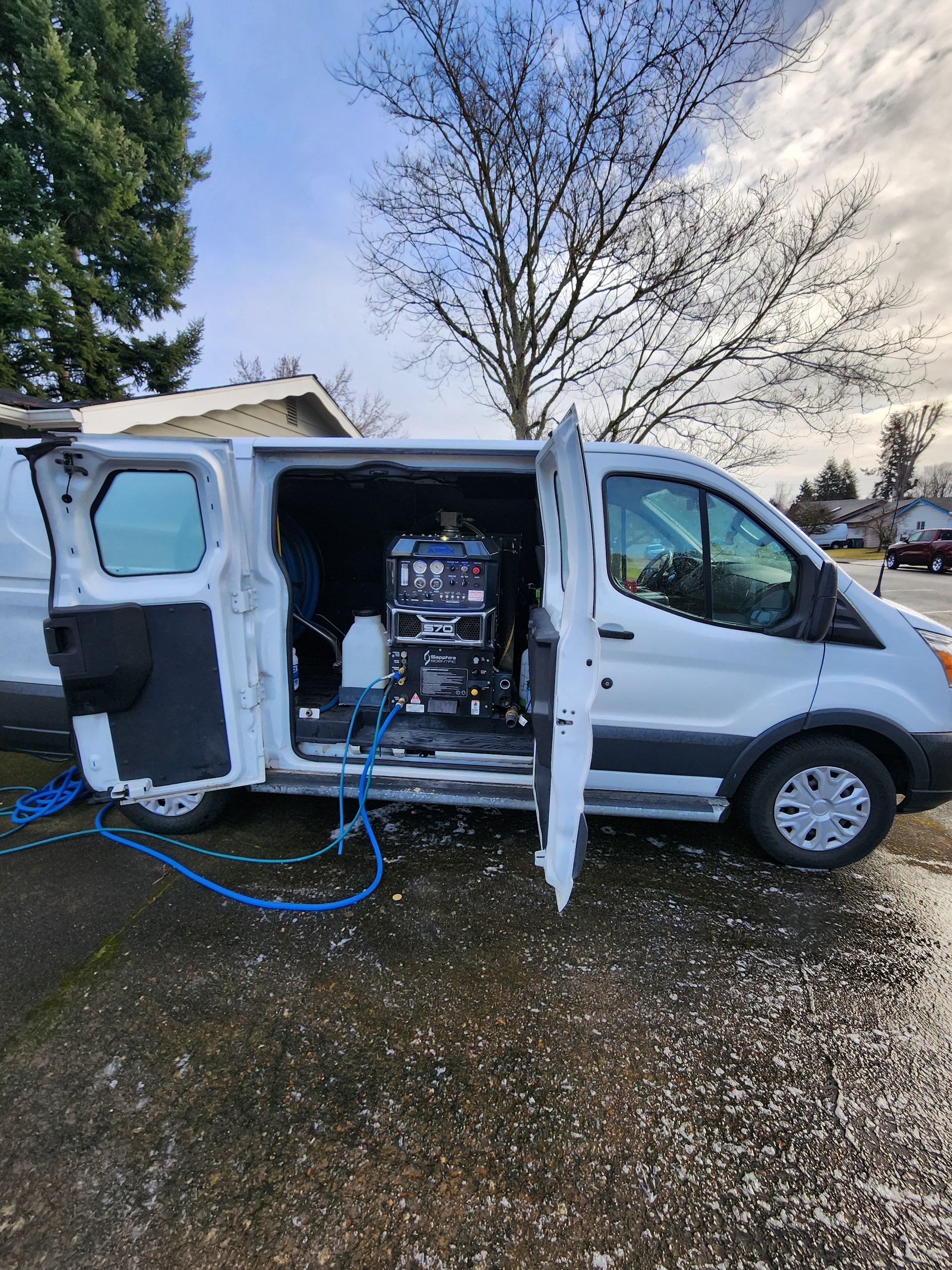 A white van with the door open is parked in a gravel lot.