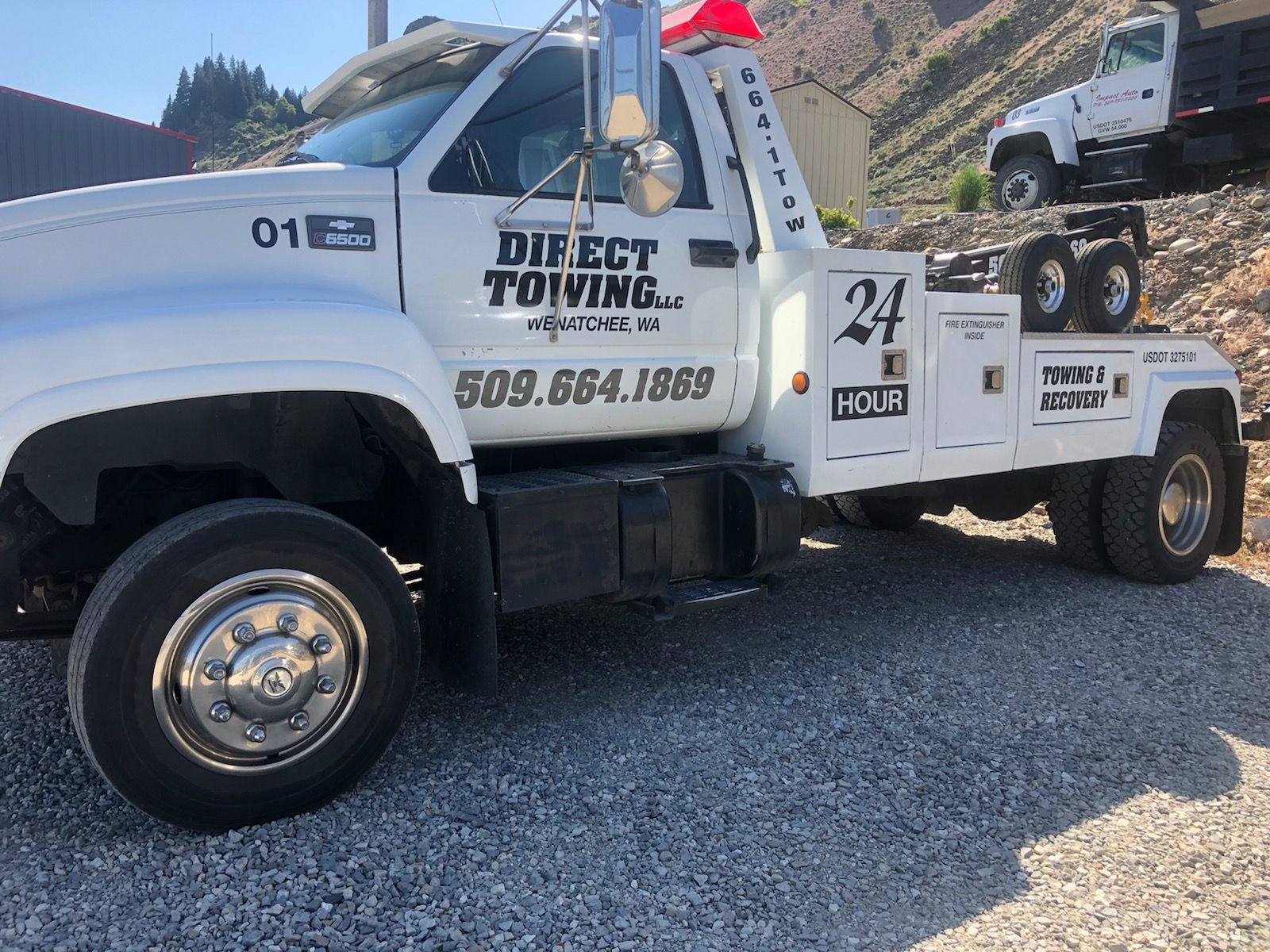 White tow truck parked on gravel, labeled Direct Towing, with mountains in the background
