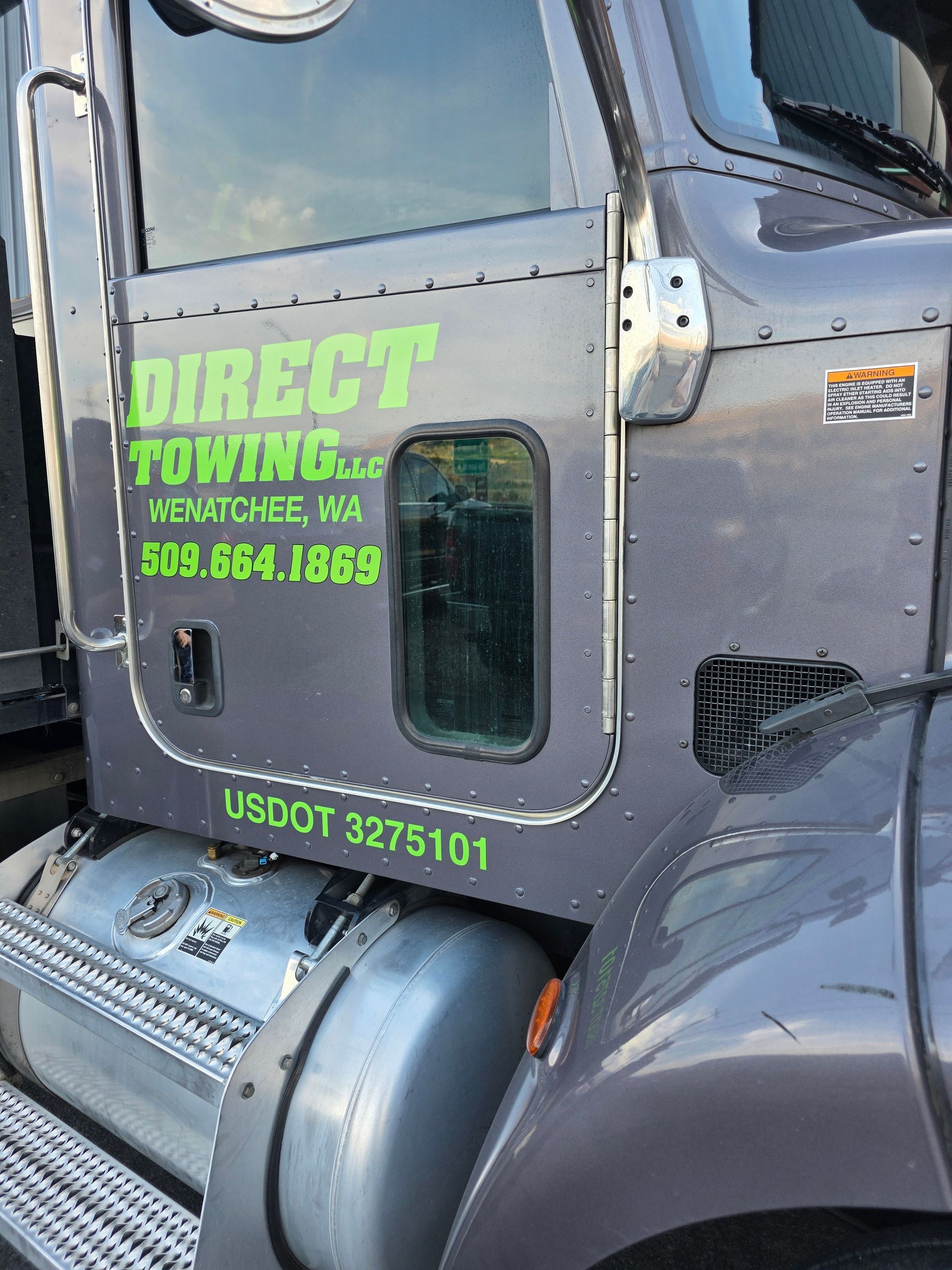 Close-up of a gray tow truck cab with neon green Direct Towing logo and contact info on the door.
