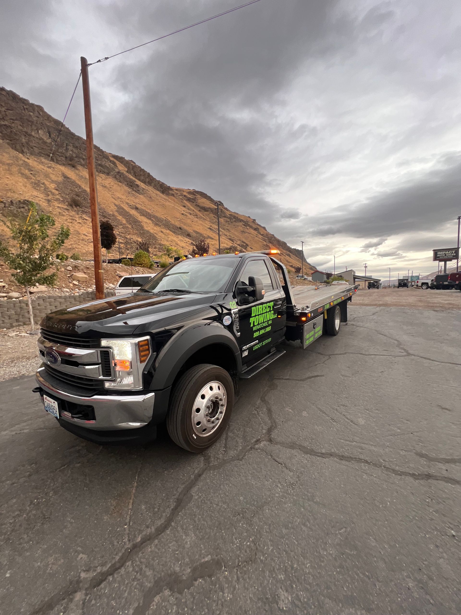 Black tow truck parked on a road beside rocky hills under a cloudy sky