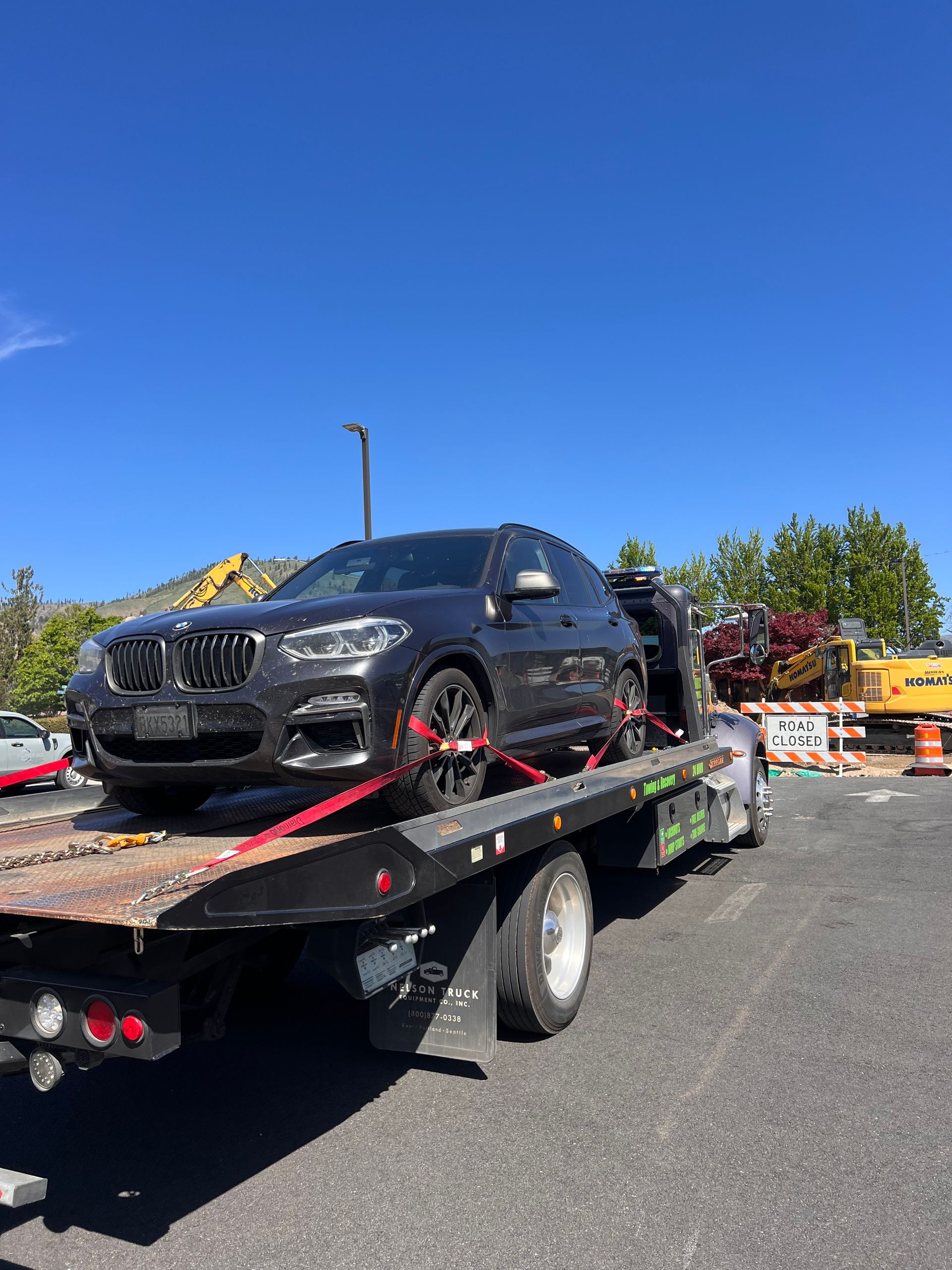 Black SUV on a flatbed tow truck parked on a sunny roadside under a clear blue sky