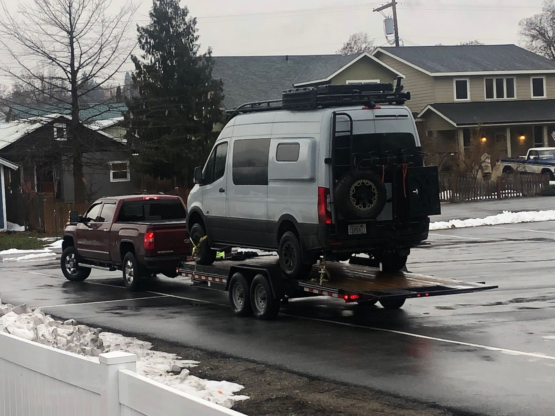 White camper van and red SUV loaded on a flatbed trailer driving on a snowy street