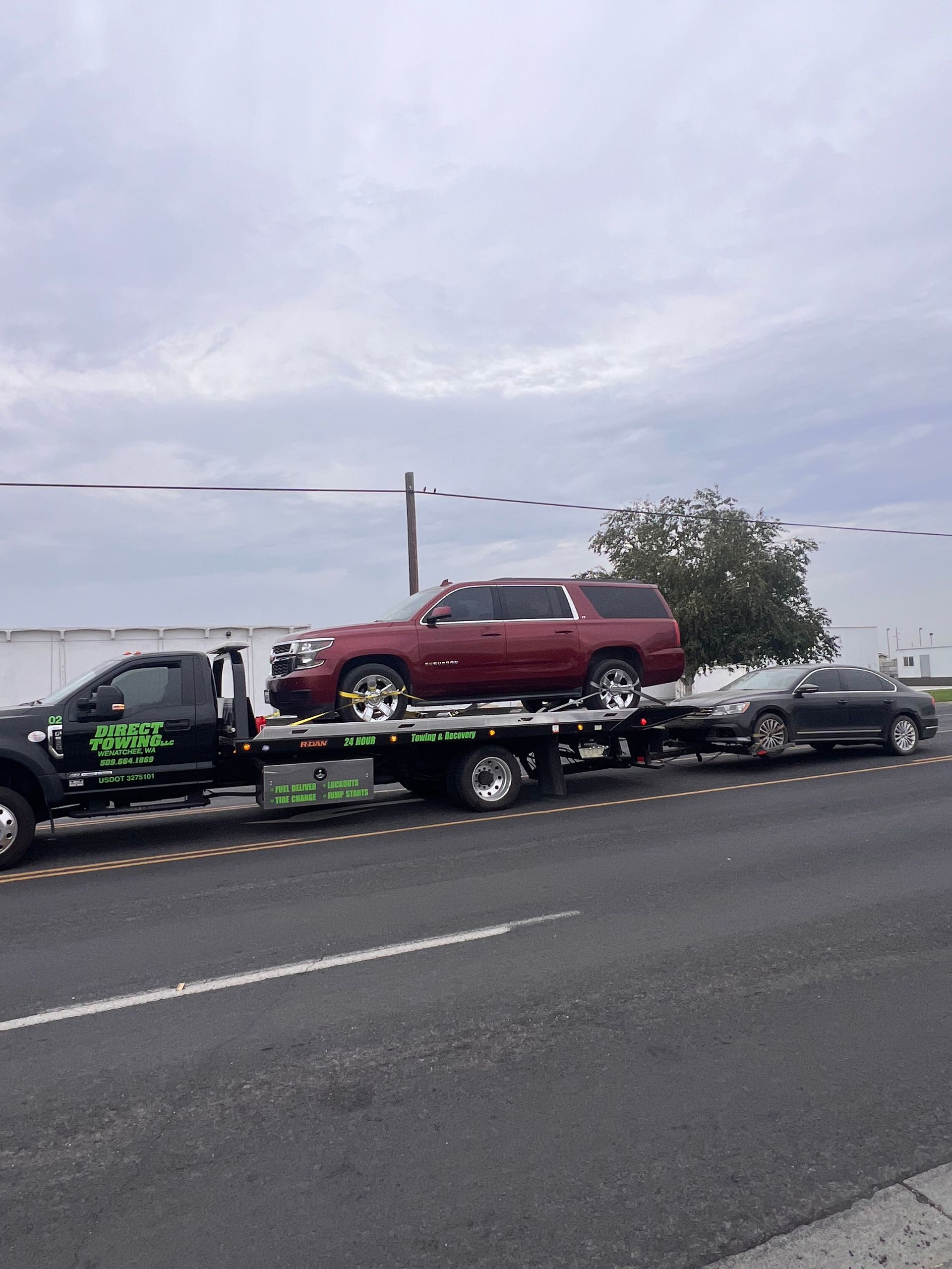 Car hauler trailer carrying a red SUV and other vehicles on a highway under cloudy skies