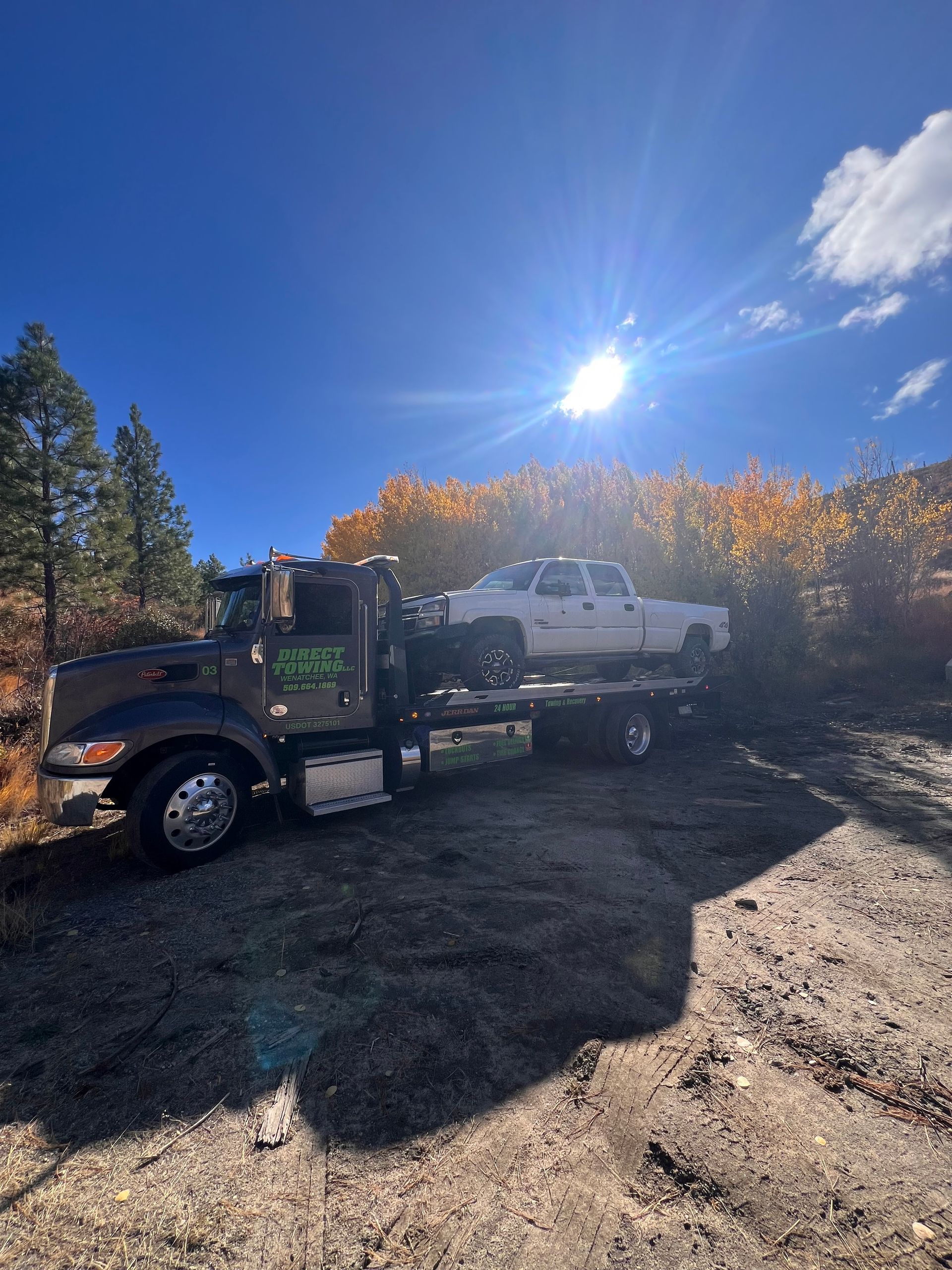 Tow truck hauling a white pickup on a gravel road under a bright blue sky