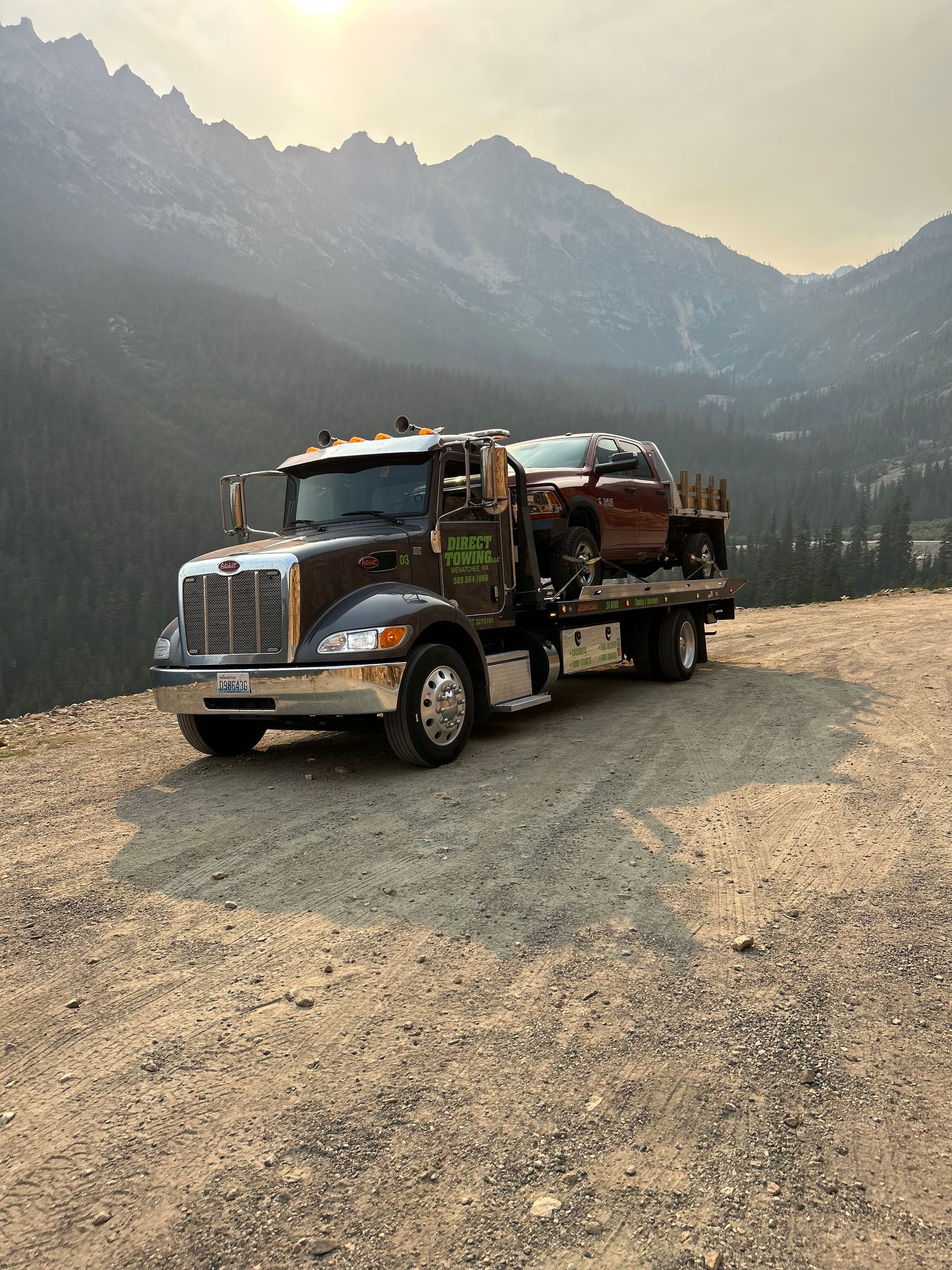 Logging truck parked on a gravel mountain road at sunrise, with forested peaks in the background