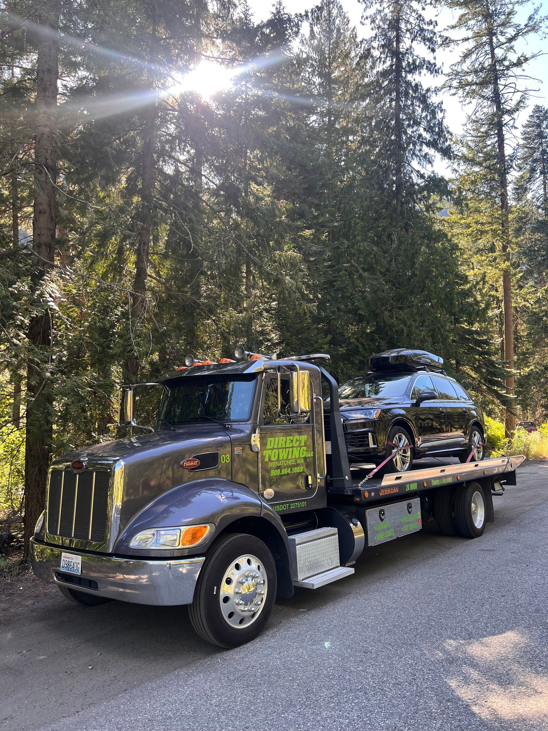 Tow truck carrying a black car on a forest road in sunlight